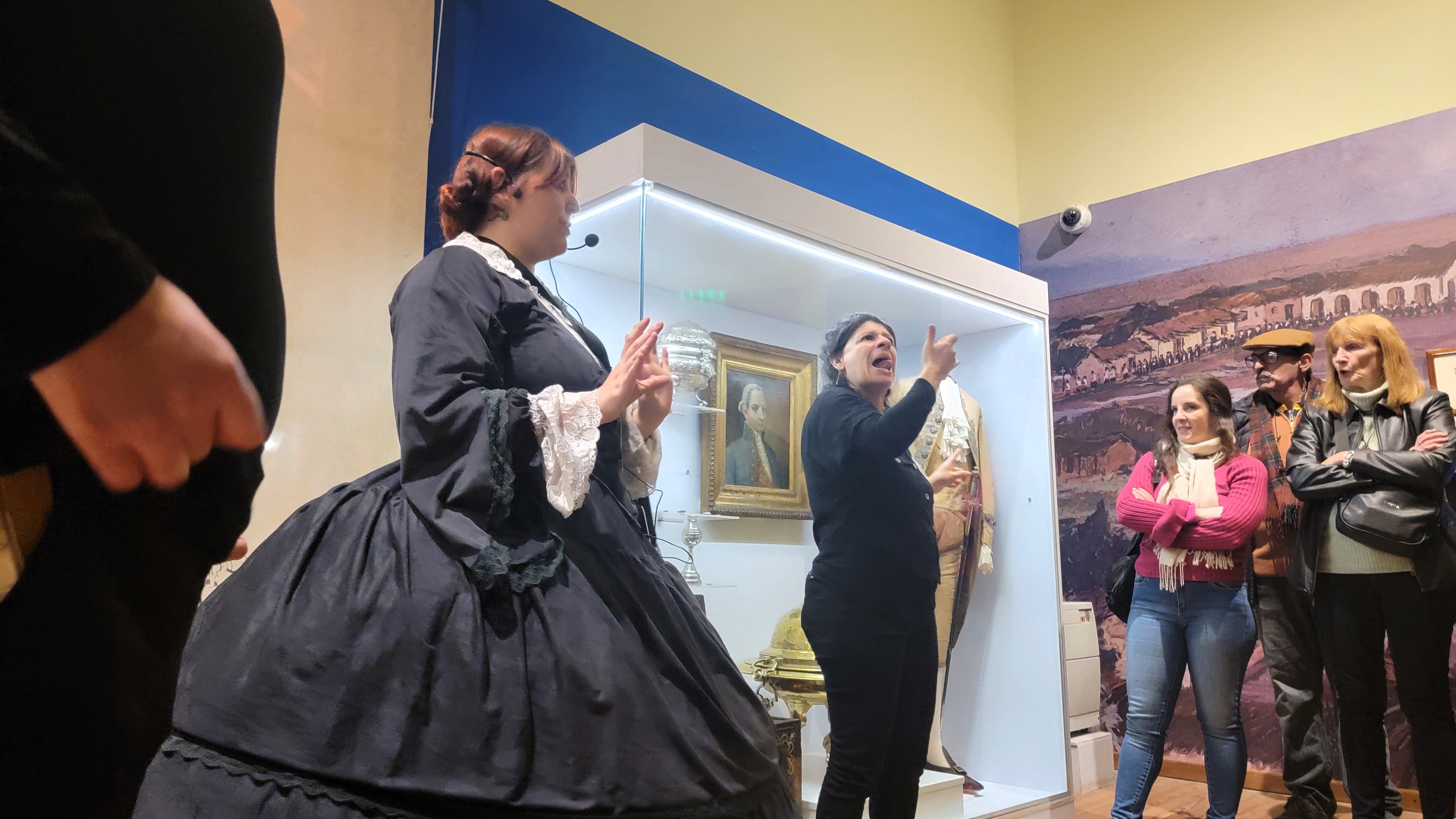 Fotografia en la que se observa en primer plano a la guia del museo vestida con traje del siglo 19 y a su izquierda interprete 