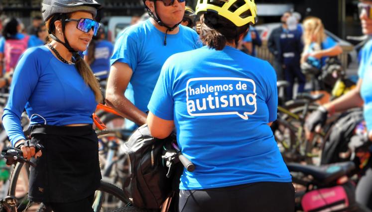 grupo de tres personas ciclistas con remera azul. En primer plano mujer de espaldas con logo blanco "hablemos de autismo"