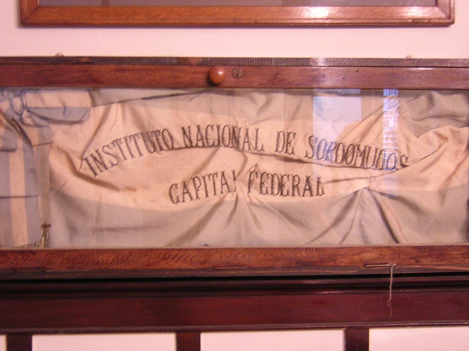 Foto:Bandera argentina(celeste y blanca) con un bordado que dice lo siguiente:"Instituto Nacional de Sordosmudos Capital Federal"