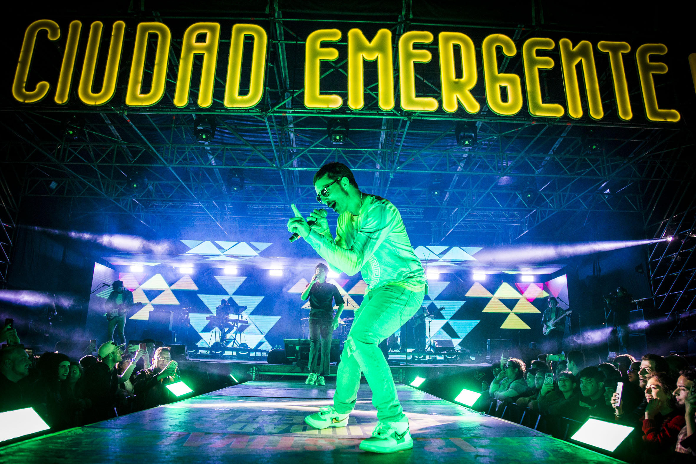 Escenario de Ciudad Emergente con cantante iluminado de verde y musicos en el escenario
