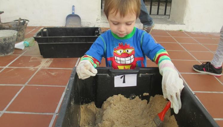 Un nene con un cajon con arena revolviendo arena con una pala 