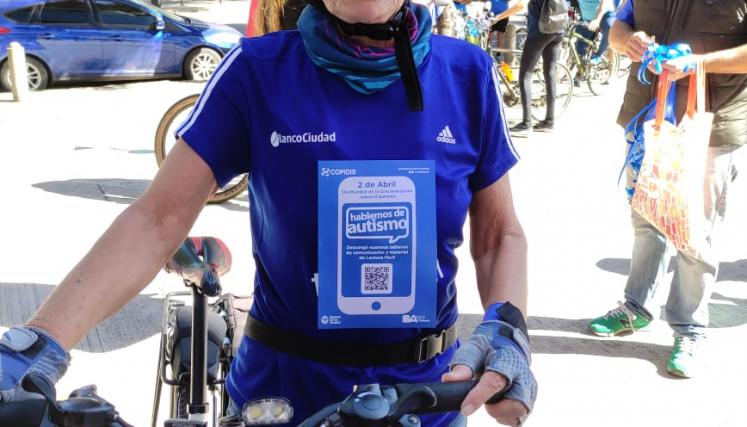 Imagen 6: Mujer de pie sosteniendo una bicicleta. Viste una remera azul, lentes y casco. Sobre la remera, el folleto de fondo azul y Letras blancas con QR
